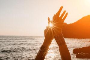 femme mer yoga. content femme dans blanc maillot de bain et boho style bracelets pratiquant en plein air sur yoga tapis par mer sur le coucher du soleil. femmes yoga aptitude routine. en bonne santé mode de vie, harmonie et méditation photo