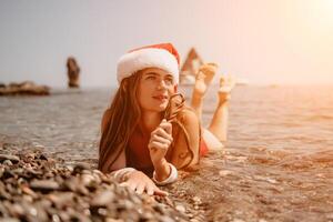 femme Voyage mer. content touristique prendre plaisir prise image sur le plage pour souvenirs. femme voyageur dans Père Noël chapeau regards à caméra sur le mer baie, partage Voyage aventure périple photo