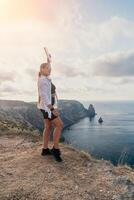 femme Voyage mer. content touristique dans chapeau prendre plaisir prise image en plein air pour souvenirs. femme voyageur posant sur le plage à mer entouré par volcanique montagnes, partage Voyage aventure périple photo