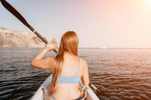 femme dans kayak retour voir. content Jeune femme avec longue cheveux flottant dans kayak sur calme mer. été vacances vacances et de bonne humeur femelle gens relaxant ayant amusement sur le bateau. photo