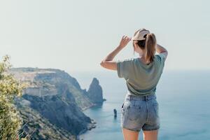 femme Voyage mer. content touristique dans chapeau prendre plaisir prise image en plein air pour souvenirs. femme voyageur posant sur le plage à mer entouré par volcanique montagnes, partage Voyage aventure périple photo