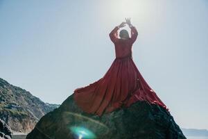 femme Voyage mer. Jeune content femme dans une longue rouge robe posant sur une plage près le mer sur Contexte de volcanique rochers, comme dans Islande, partage Voyage aventure périple photo