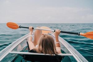 femme dans kayak retour voir. content Jeune femme avec longue cheveux flottant dans transparent kayak sur le cristal clair mer. été vacances vacances et de bonne humeur femelle gens relaxant ayant amusement sur le bateau photo