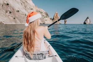 femme dans kayak retour voir. content Jeune femme dans Père Noël chapeau flottant dans kayak sur calme mer. été vacances vacances et de bonne humeur femelle gens relaxant ayant amusement sur le bateau. photo