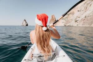 femme dans kayak retour voir. content Jeune femme dans Père Noël chapeau flottant dans kayak sur calme mer. été vacances vacances et de bonne humeur femelle gens relaxant ayant amusement sur le bateau. photo