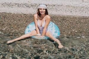 femme été mer. content femme nager avec gonflable Donut sur le plage dans été ensoleillé jour, entouré par volcanique montagnes. été vacances concept. photo