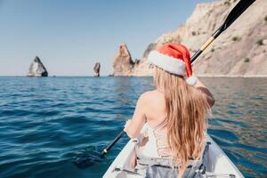 femme dans kayak retour voir. content Jeune femme dans Père Noël chapeau flottant dans kayak sur calme mer. été vacances vacances et de bonne humeur femelle gens relaxant ayant amusement sur le bateau. photo