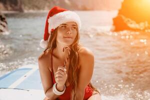 femme Voyage mer. content touristique prendre plaisir prise image sur le plage pour souvenirs. femme voyageur dans Père Noël chapeau regards à caméra sur le mer baie, partage Voyage aventure périple photo