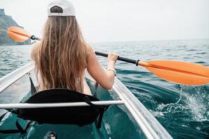 femme dans kayak retour voir. content Jeune femme avec longue cheveux flottant dans transparent kayak sur le cristal clair mer. été vacances vacances et de bonne humeur femelle gens relaxant ayant amusement sur le bateau photo