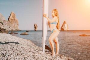 femme mer souper. proche en haut portrait de content Jeune caucasien femme avec longue cheveux à la recherche à caméra et souriant. mignonne femme portrait dans une bleu bikini posant sur souper planche dans le mer photo