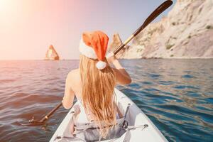 femme dans kayak retour voir. content Jeune femme dans Père Noël chapeau flottant dans kayak sur calme mer. été vacances vacances et de bonne humeur femelle gens relaxant ayant amusement sur le bateau. photo