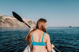 femme dans kayak retour voir. content Jeune femme avec longue cheveux flottant dans kayak sur calme mer. été vacances vacances et de bonne humeur femelle gens relaxant ayant amusement sur le bateau. photo