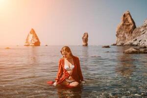 femme Voyage mer. content touristique dans rouge robe prendre plaisir prise image en plein air pour souvenirs. femme voyageur posant dans mer plage, entouré par volcanique montagnes, partage Voyage aventure périple photo