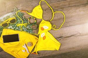 ensemble de plage vêtements Jaune bikini, bracelets, shorts, des lunettes sur foncé en bois Contexte. Haut voir. été vacances concept. photo