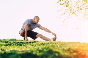 Jeune athlétique coureur Faire élongation exercer, en train de préparer pour faire des exercices dans le parc. le coucher du soleil photo