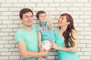 content et souriant Jeune famille portrait sur brique mur Contexte. père et mère avec peu bébé garçon. Parents avec enfant photo