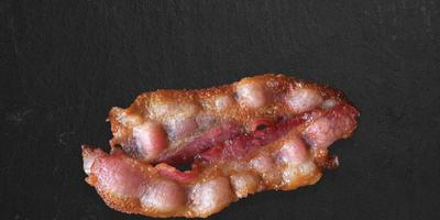 tranches de bacon fumé à coupe épaisse et croustillantes isolées sur fond sombre, vue rapprochée adaptée au projet de conception de produits alimentaires. photo