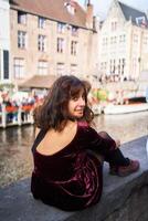 une fille dans une rouge velours côtelé robe avec un ouvert retour des promenades par le des rues de Bruges sur un l'automne journée photo