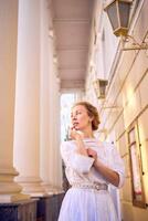 élégant milieu âge femme dans blanc ancien robe près théâtre avec antique colonnades photo