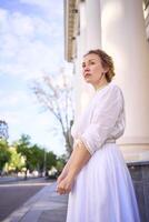 élégant milieu âge femme dans blanc ancien robe près théâtre avec antique colonnades photo