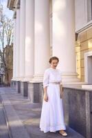 élégant milieu âge femme dans blanc ancien robe près théâtre avec antique colonnades photo
