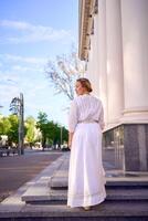 élégant milieu âge femme dans blanc ancien robe près théâtre avec antique colonnades photo