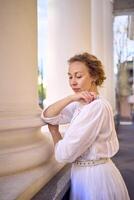 élégant milieu âge femme dans blanc ancien robe près théâtre avec antique colonnades photo