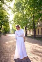 élégant milieu âge femme dans une blanc ancien robe dans une ensoleillé ruelle photo