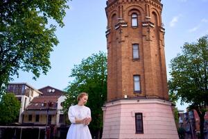 élégant Jeune femme dans une blanc ancien robe sur le carré près le historique l'eau la tour dans vinnytsia photo