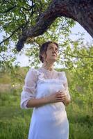 magnifique femme dans blanc ancien robe avec train dans printemps jardin à le coucher du soleil photo