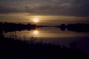 une homme dans une kayak dans le milieu de une Lac à le coucher du soleil photo