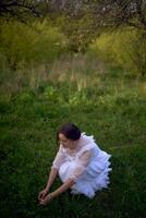 magnifique femme dans blanc ancien robe avec train dans printemps jardin à le coucher du soleil photo