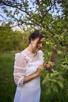 magnifique femme dans blanc ancien robe avec train dans printemps jardin à le coucher du soleil photo