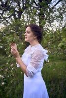 magnifique femme dans blanc ancien robe avec train dans printemps jardin à le coucher du soleil photo