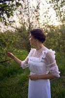 magnifique femme dans blanc ancien robe avec train dans printemps jardin à le coucher du soleil photo