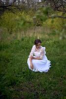 magnifique femme dans blanc ancien robe avec train dans printemps jardin à le coucher du soleil photo