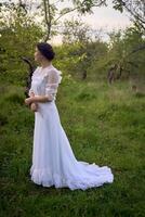 magnifique femme dans blanc ancien robe avec train dans printemps jardin à le coucher du soleil photo