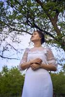 magnifique femme dans blanc ancien robe avec train dans printemps jardin à le coucher du soleil photo