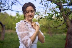 magnifique femme dans blanc ancien robe avec train dans printemps jardin à le coucher du soleil photo