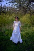 magnifique femme dans blanc ancien robe avec train dans printemps jardin à le coucher du soleil photo