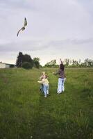 deux peu sœurs et mère courir et lancement une cerf-volant dans une champ photo