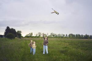 deux peu sœurs et mère courir et lancement une cerf-volant dans une champ photo