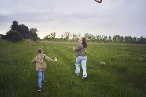 deux peu sœurs et mère courir et lancement une cerf-volant dans une champ photo