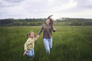 deux peu sœurs et mère courir et lancement une cerf-volant dans une champ photo