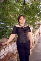 une moyen Taille femme dans une noir corset et large jambe pantalon des promenades par le ville dans le Matin lumière photo