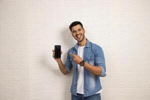 bien homme montrer du doigt à le sien téléphone avec une sourire photo