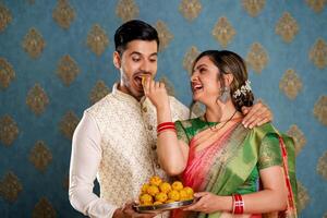 une Stock photo de une mignonne romantique couple profiter laddus à le diwali fête tandis que habillé traditionnellement