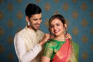 image de agréable couple habillé dans traditionnel Indien tenue attacher ou en présentant Collier à le sien épouse photo