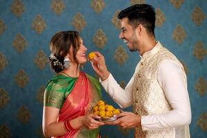 une image spectacles une sucré couple en mangeant laddus tandis que habillé dans traditionnel Indien tenue pour le Festival de diwali photo