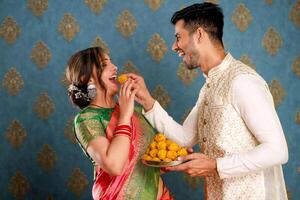 Jeune romantique couple dans Indien ethnique porter en mangeant laddu sur diwali occasion. photo